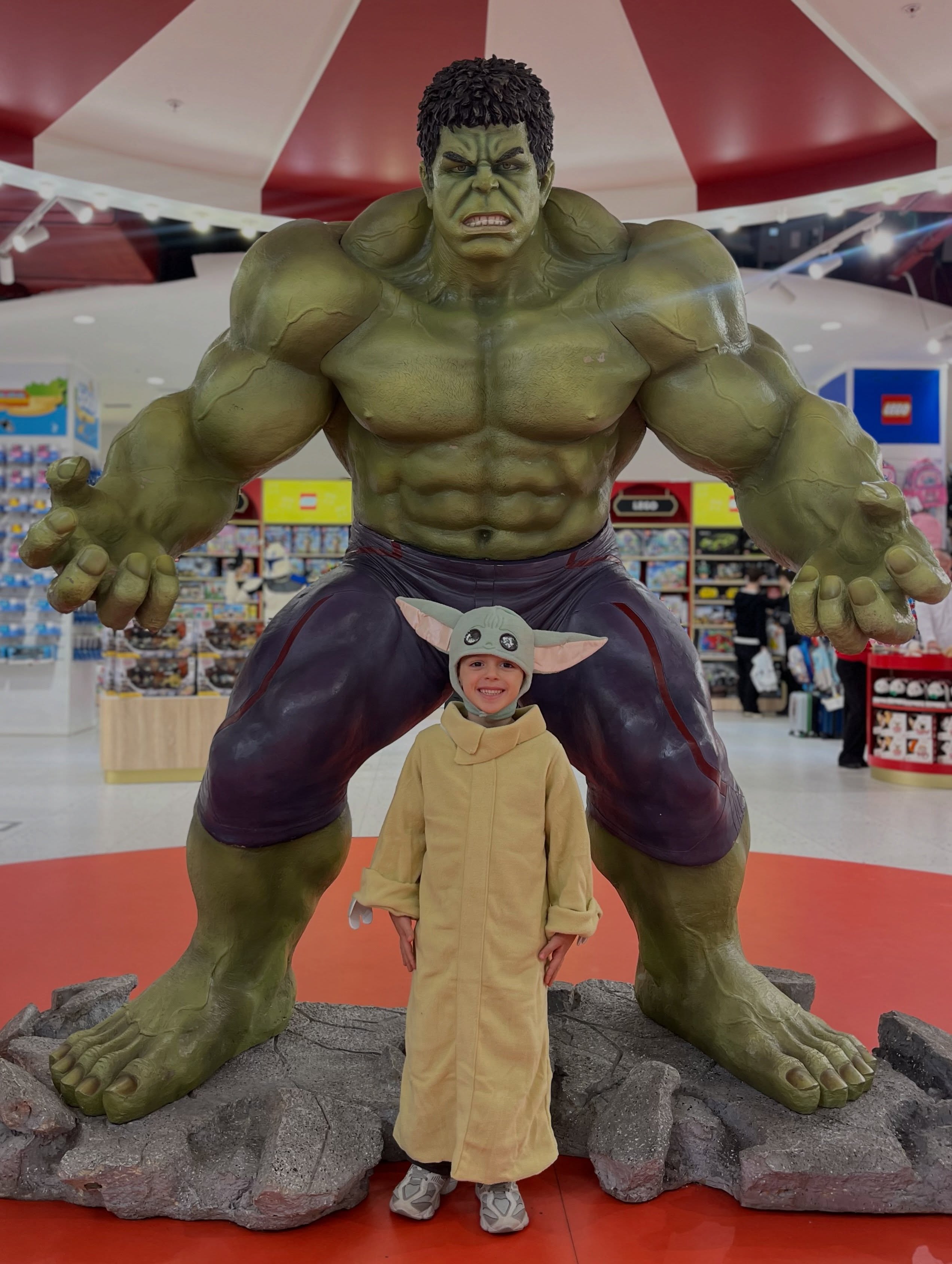 Fëmijë me kostum pranë statujës së Hulk – Hamleys Kosova