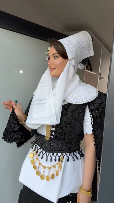 Veshje tradicionale nusërie me jelek të zi dhe monedha